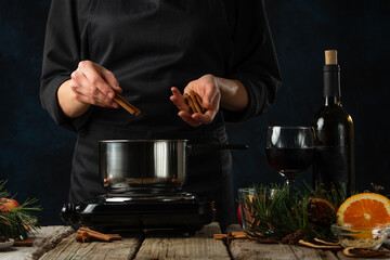 Close-up view of chef pours cinnamon into the pot for preparing mulled wine on rustic wooden table with festive composition background. Backstage of cooking hot drink with spices. Frozen motion.