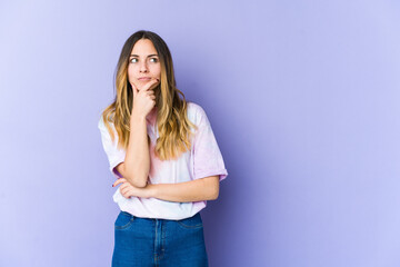 Young caucasian woman isolated on purple background looking sideways with doubtful and skeptical expression.