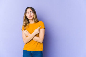 Young caucasian woman isolated on purple background points sideways, is trying to choose between two options.