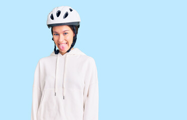 Beautiful brunette young woman wearing bike helmet and sporty clothes sticking tongue out happy with funny expression. emotion concept.
