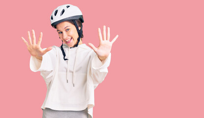 Beautiful brunette young woman wearing bike helmet and sporty clothes showing and pointing up with fingers number ten while smiling confident and happy.