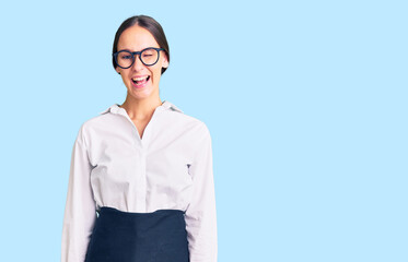 Beautiful brunette young woman wearing professional waitress apron winking looking at the camera...