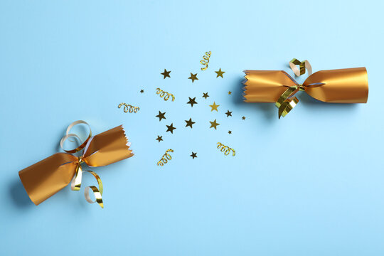 Open golden Christmas cracker with shiny confetti on light blue background, top view