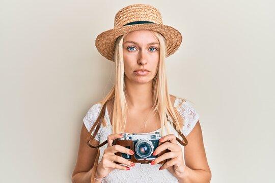 Young blonde girl wearing summer hat using camera relaxed with serious expression on face. simple and natural looking at the camera.