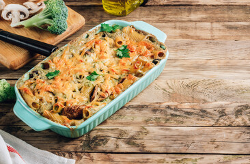 Casserole with pasta, mushrooms, broccoli sauce and cheese on a rustic wooden background.
