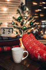 Feet in Christmas socks. Close up on feet. Winter and Christmas holidays concept. The cup of hot drink. Cozy scene. Background with christmas decor. Christmas background.