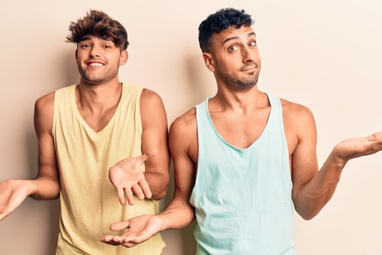Young gay couple wearing casual clothes clueless and confused expression with arms and hands raised. doubt concept.