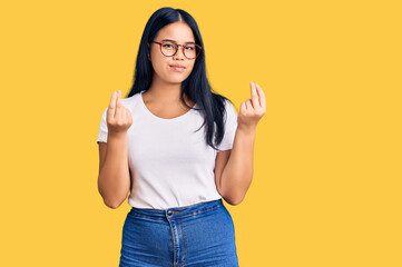 Young beautiful asian girl wearing casual clothes and glasses doing money gesture with hands, asking for salary payment, millionaire business