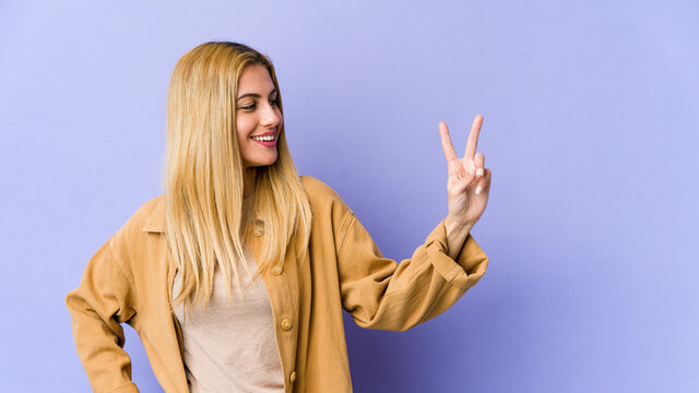 Young blonde caucasian woman joyful and carefree showing a peace symbol with fingers.