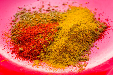 Spices - red pepper, ground coriander, salt and turmeric on a red plate, close-up