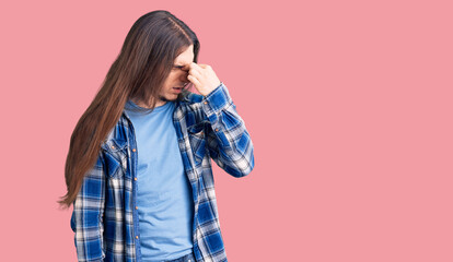 Young adult man with long hair wearing casual shirt tired rubbing nose and eyes feeling fatigue and headache. stress and frustration concept.