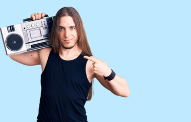 Young adult man with long hair wearing black clothes and holding boombox pointing finger to one...