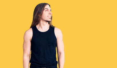 Obraz premium Young adult man with long hair wearing rocker style with black clothes and contact lenses looking away to side with smile on face, natural expression. laughing confident.