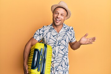 Handsome muscle man holding suitcase going on summer vacation celebrating achievement with happy smile and winner expression with raised hand