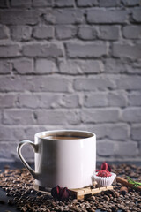 White cup full of coffee beans , red flowers and red chocolate candy against the background of a dark brick wall. Morning espresso. Coffee mug.	
