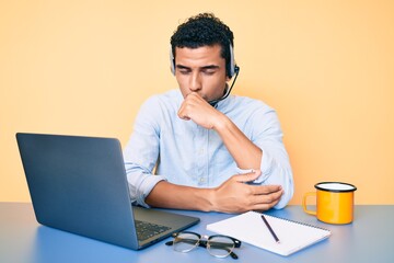 Young handsome hispanic man working at the office wearing operator headset feeling unwell and...