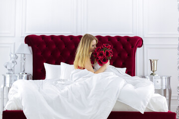 Chic blonde woman in luxury white with red bedroom. Rich expensive interior.
