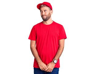 Young handsome blond man wearing t-shirt and cap smiling looking to the side and staring away thinking.