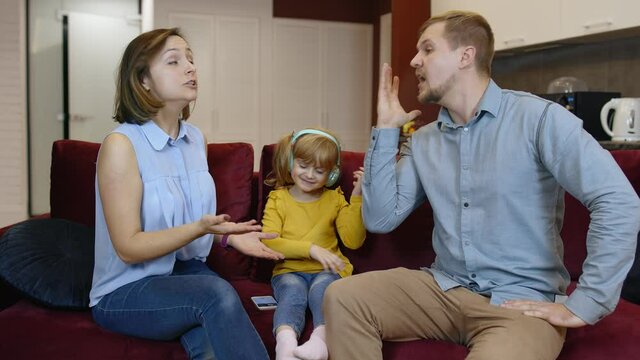 Caucasian child girl kid trying to be distracted and not hear quarrels between parents at home. Angry man and woman quarrelling and fighting in living room. Family problems conflict, crisis. Parenting