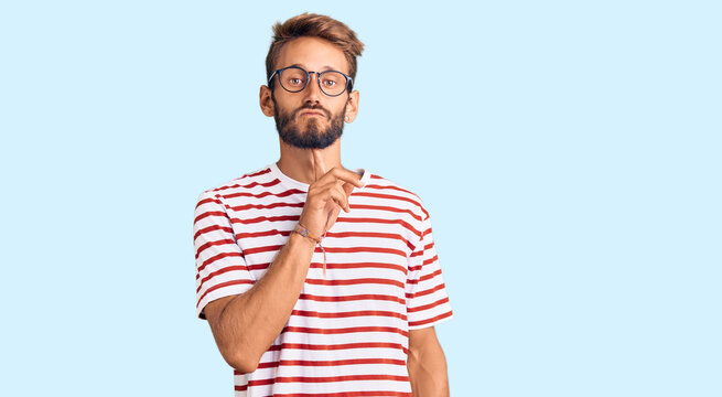 Handsome blond man with beard wearing casual clothes and glasses thinking concentrated about doubt with finger on chin and looking up wondering
