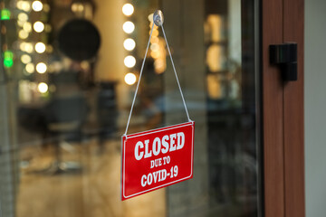 Red sign with words Closed Due To Covid-19 hanging on glass door