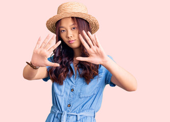 Young beautiful chinese girl wearing summer hat doing frame using hands palms and fingers, camera...