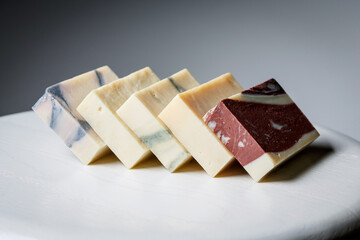 Natural handmade soap bars with different ingredients on a white wooden background.