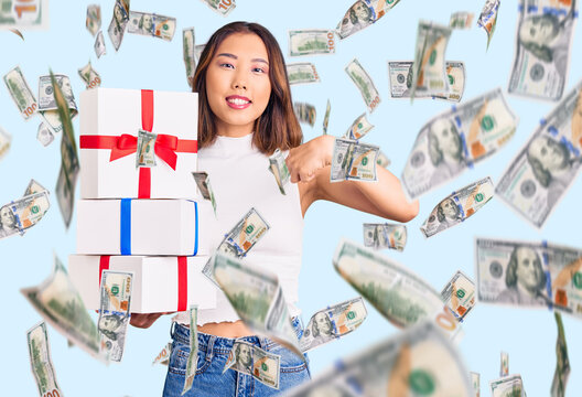 Young beautiful chinese girl holding gift pointing finger to one self smiling happy and proud