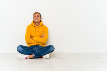 Obraz na płótnie Canvas Young caucasian man sitting on the floor who feels confident, crossing arms with determination.