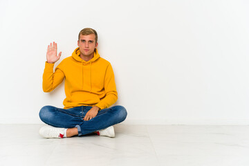 Fototapeta na wymiar Young caucasian man sitting on the floor smiling cheerful showing number five with fingers.