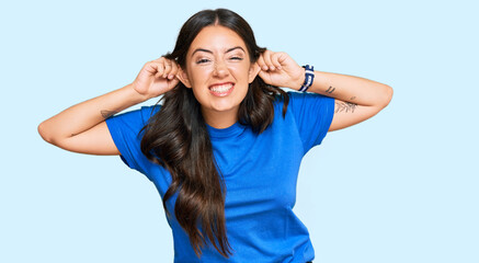 Beautiful brunette young woman wearing casual clothes smiling pulling ears with fingers, funny...