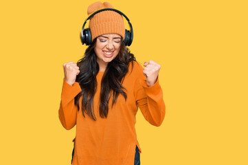 Beautiful brunette young woman listening to music using headphones excited for success with arms raised and eyes closed celebrating victory smiling. winner concept.