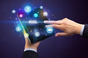 Businessman holding a foldable smartphone with #COOL inscription, social media concept