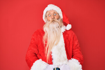 Old senior man with grey hair and long beard wearing traditional santa claus costume making fish face with lips, crazy and comical gesture. funny expression.