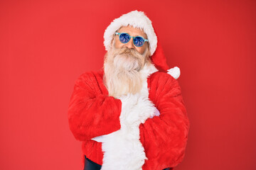 Old senior man wearing santa claus costume and sunglasses happy face smiling with crossed arms looking at the camera. positive person.