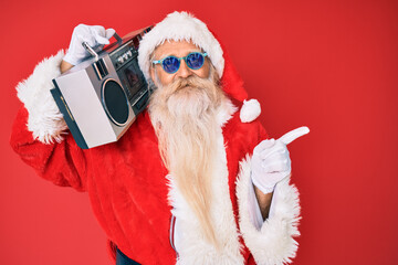 Old senior man wearing santa claus costume and boombox smiling happy pointing with hand and finger to the side