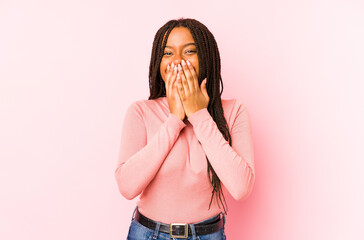 Young african american woman isolated on a pink background laughing about something, covering mouth with hands.