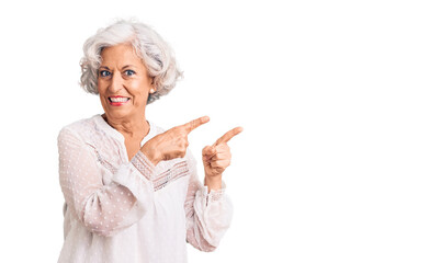 Senior grey-haired woman wearing casual clothes smiling and looking at the camera pointing with two hands and fingers to the side.