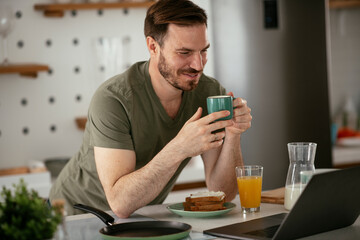 Young man eating breakfast and reading the news online. Handsome man enjoying at home..
