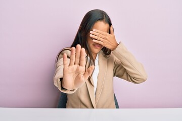 Beautiful hispanic woman working at the office covering eyes with hands and doing stop gesture with sad and fear expression. embarrassed and negative concept.