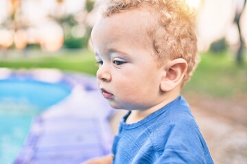 Cute and happy little boy having fun at the park on a sunny day. Beautiful blonde hair male toddler playing outdoors