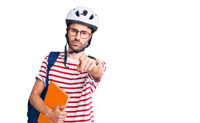 Young hispanic man wearing student backpack and bike helmet holding binder pointing with finger to the camera and to you, confident gesture looking serious