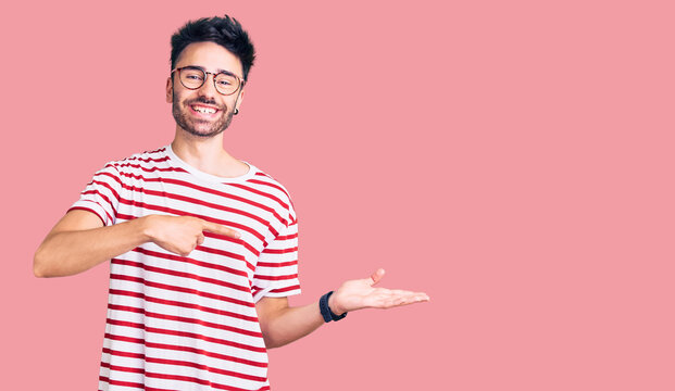 Young hispanic man wearing casual clothes amazed and smiling to the camera while presenting with hand and pointing with finger.