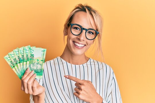 Beautiful blonde woman holding south african 10 rand banknotes smiling happy pointing with hand and finger