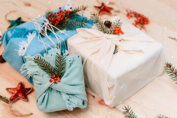 Obraz na płótnie Canvas Zero waste christmas concept. Gift boxes wrapped in fabric with spruce branch and berries on wooden background. Flatlay. Eco friendly Sustainable lifestile. No plastic. Selective focus. Copy space.