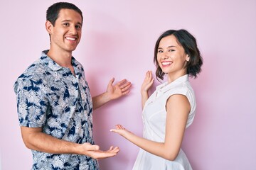 Beautiful couple wearing casual clothes inviting to enter smiling natural with open hand