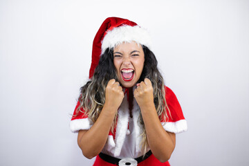 Young beautiful woman wearing a Santa Claus costume over white background very happy and excited making winner gesture with raised arms, smiling and screaming for success.