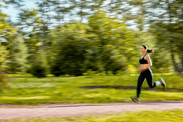 Blurred motion of running active woman in public park.