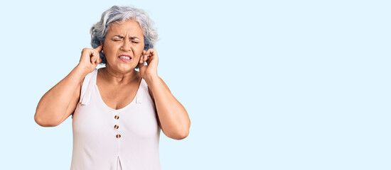 Senior woman with gray hair wearing casual clothes covering ears with fingers with annoyed expression for the noise of loud music. deaf concept.