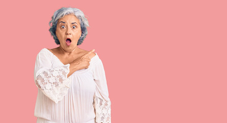 Senior woman with gray hair wearing bohemian style surprised pointing with finger to the side, open...